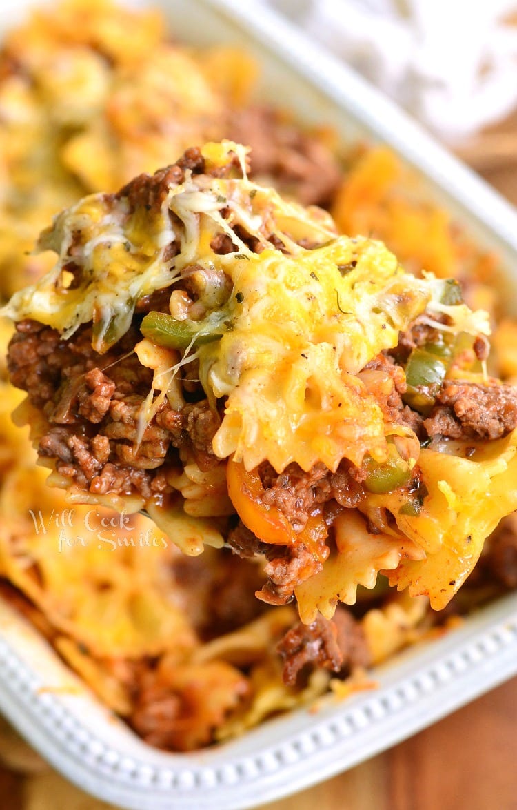 holding a ladleful of pasta casserole with ground beef, peppers and cheese.