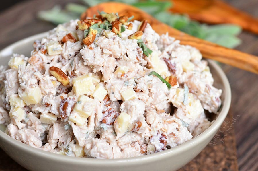 Pecan, Sage, and Gruyere Turkey Salad in a white bowl on a wood cutting board with a wood spoon