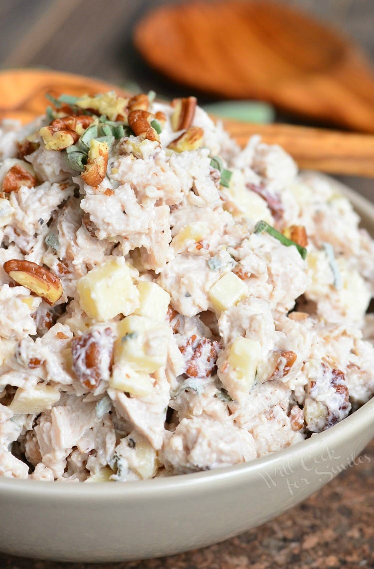 Pecan, Sage, and Gruyere Turkey Salad in white bowl with wooden spoons in the background