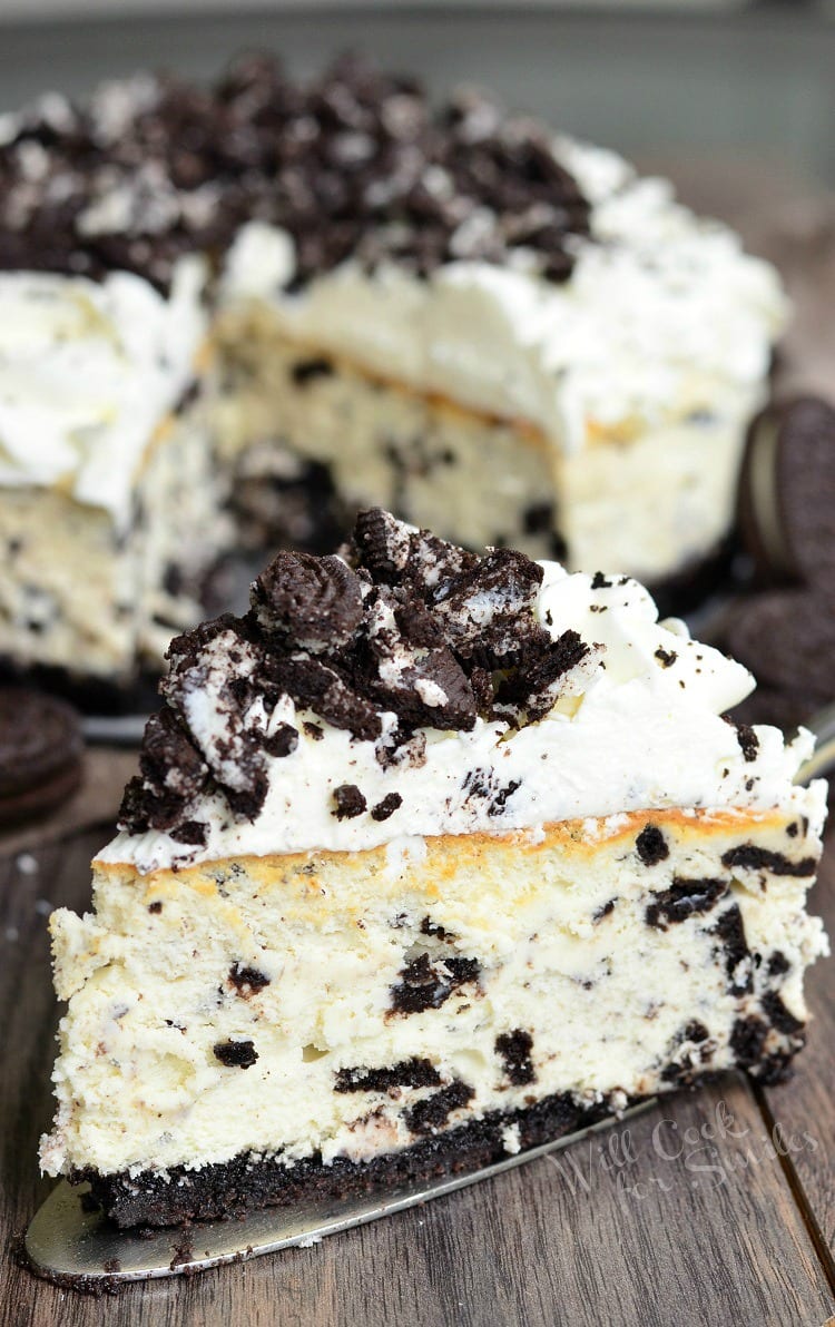 Slice of oreo cheesecake on a table with the rest of the cheesecake in the background