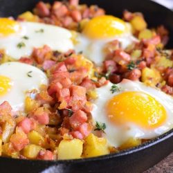 ham and potato mixture in a skillet topped with four eggs.