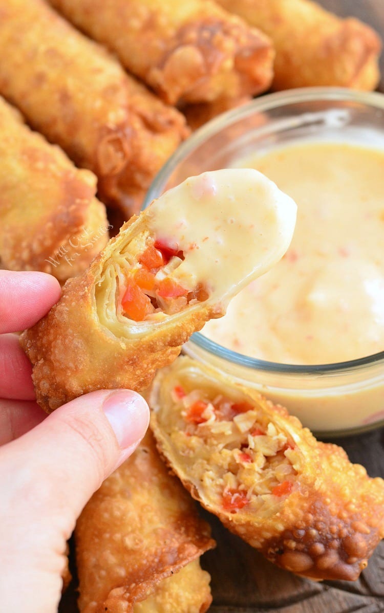 dipping Sweet Chili Chicken Egg Rolls in a Creamy Sweet Chili Sauce that is in a clear glass bowl