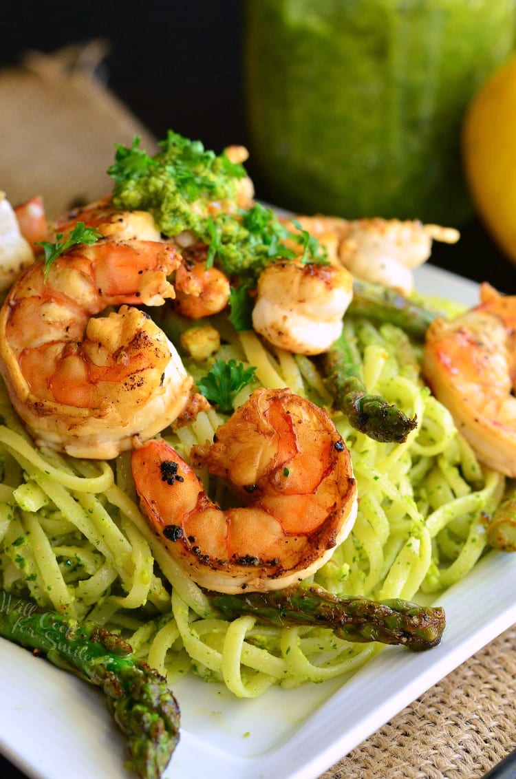 lemon pistachio pesto pasta topped with sauteed shrimp and asparagus on white plate.