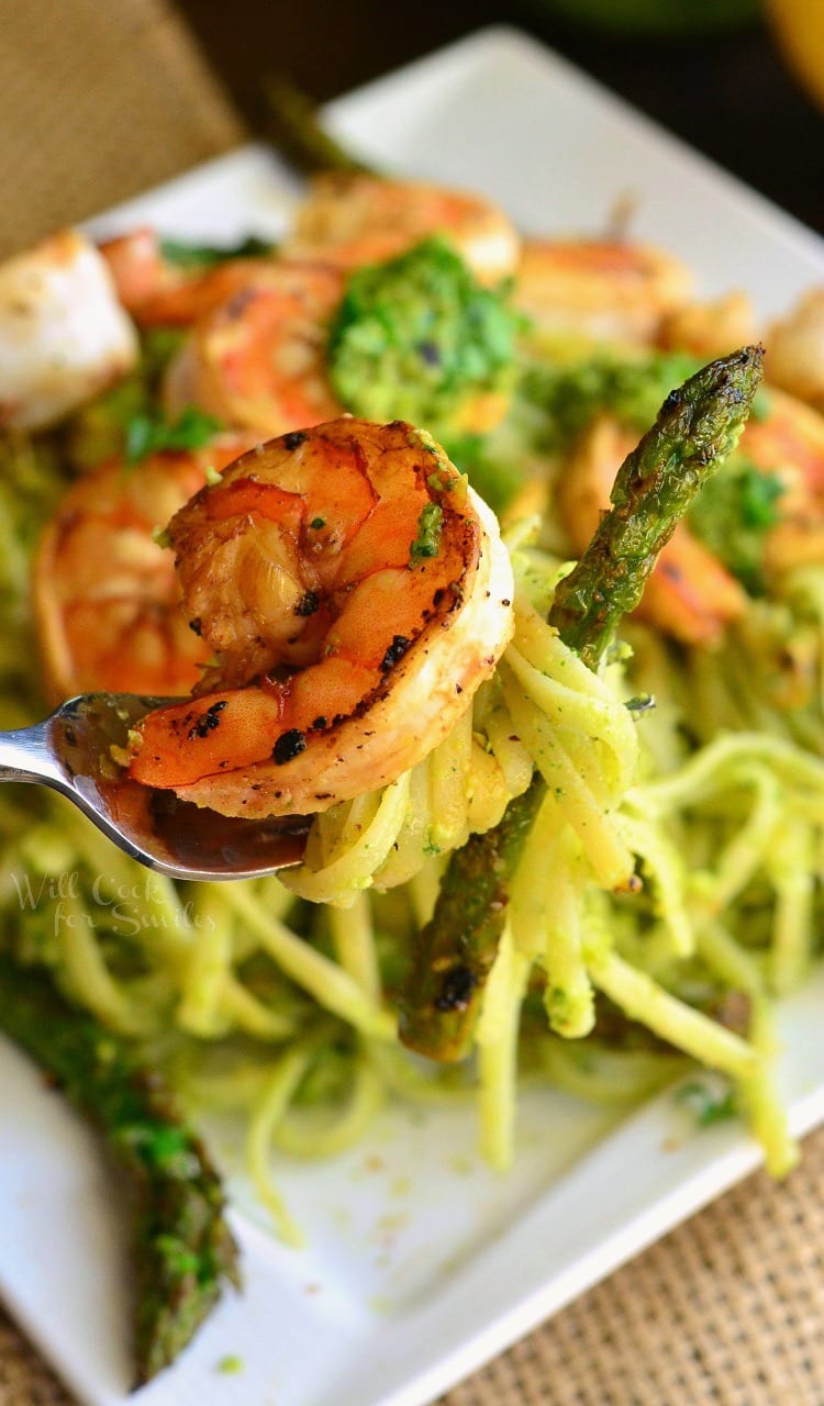holding a sauteed shrimp and asparagus with wrapped pasta on a fork over the plate.