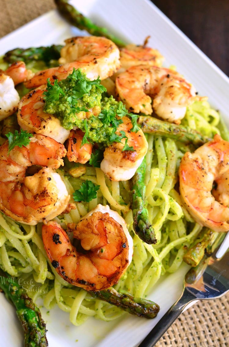 bright pesto pasta topped with sauteed shrimp and asparagus on a white plate.