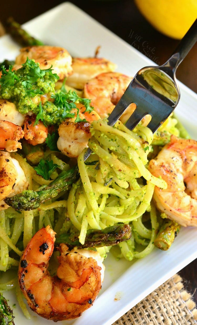 swirling some pesto pasta onto a fork from a plate with pasta and shrimp.