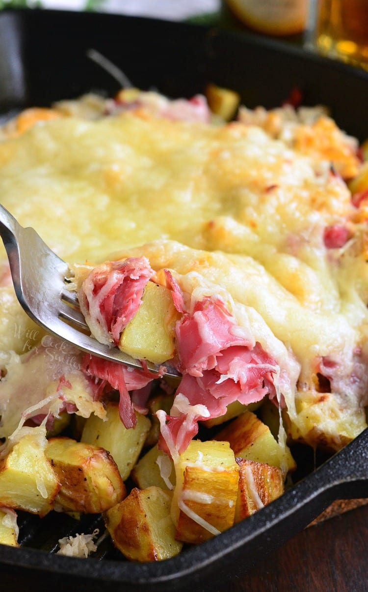 Reuben Loaded Roasted Potatoes with cheese on top in a cast iron skillet with a fork scooping some out
