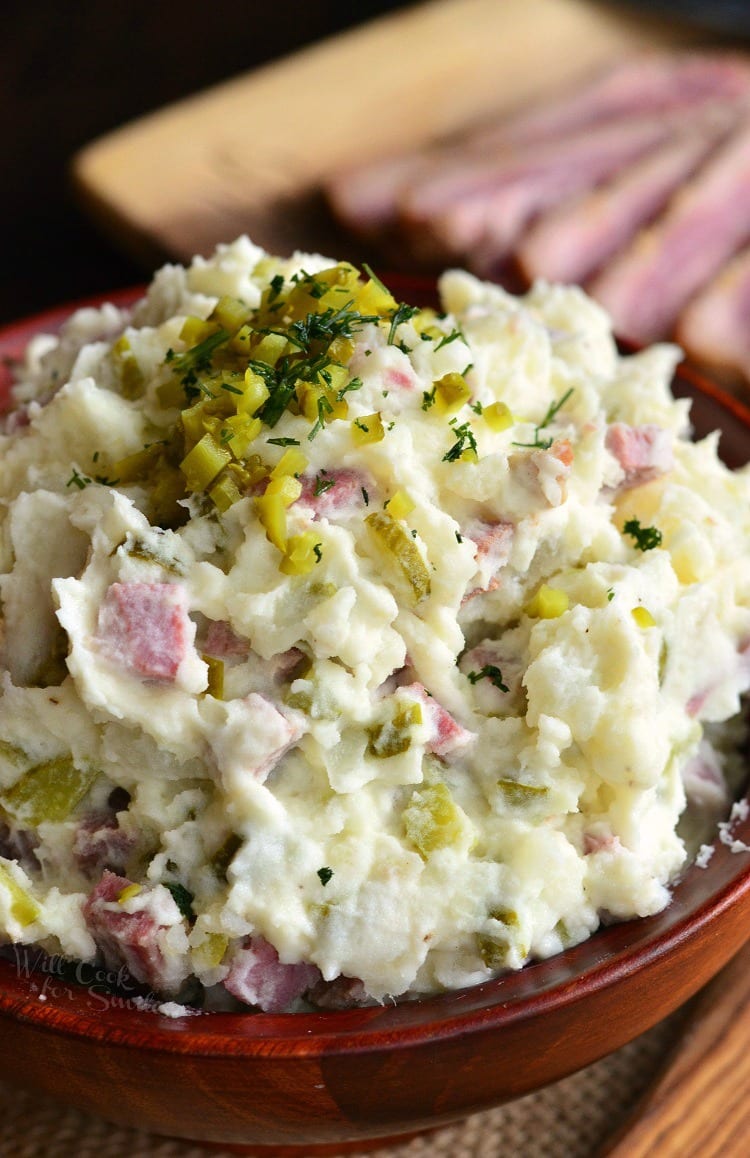 a wooden bowl filled with corned beef potato salad and topped with pickles and dill.