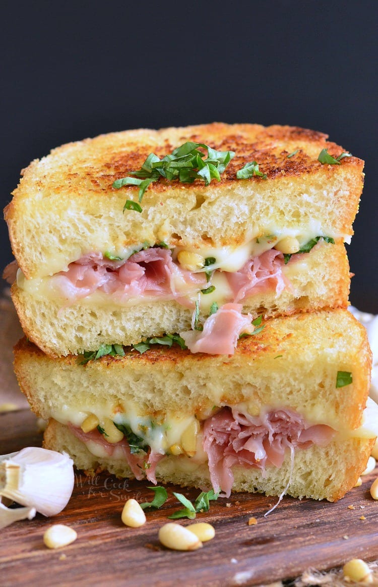 two halves of Italian grilled cheese with prosciutto stacked on cutting board.