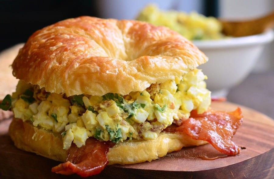 horizontal image of Bacon and Green Onion Egg Salad on a croissant on a cutting board