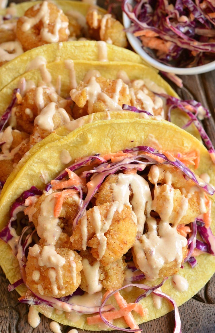 three Corn tortilla with crispy shrimp and cabbage on a wood cutting board