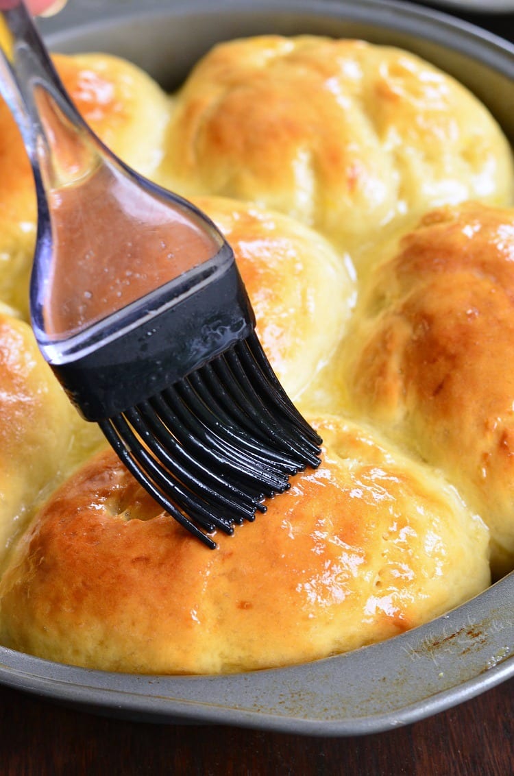 brushing Honey Lemon Dinner Rolls in a baking dish with butter
