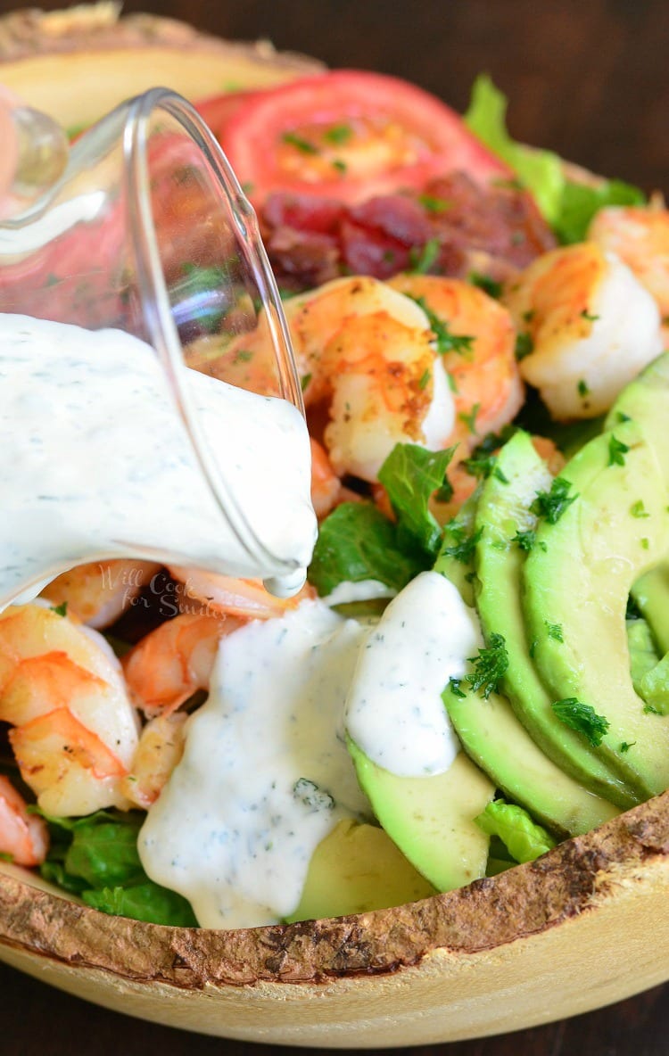 pouring ranch over Shrimp BLTA Salad that's in a bowl