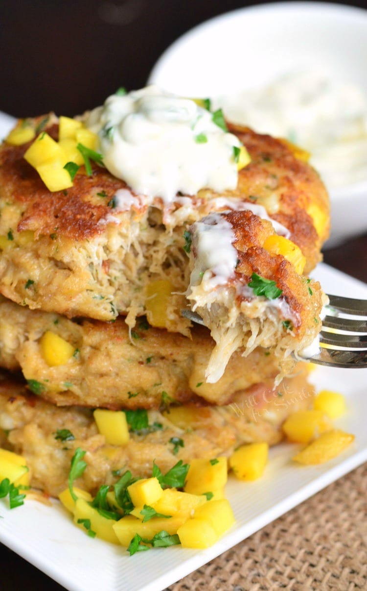 Spicy Mango Crab Cakes stacked on a plate with sour cream on top and diced mango and parsley on the plate