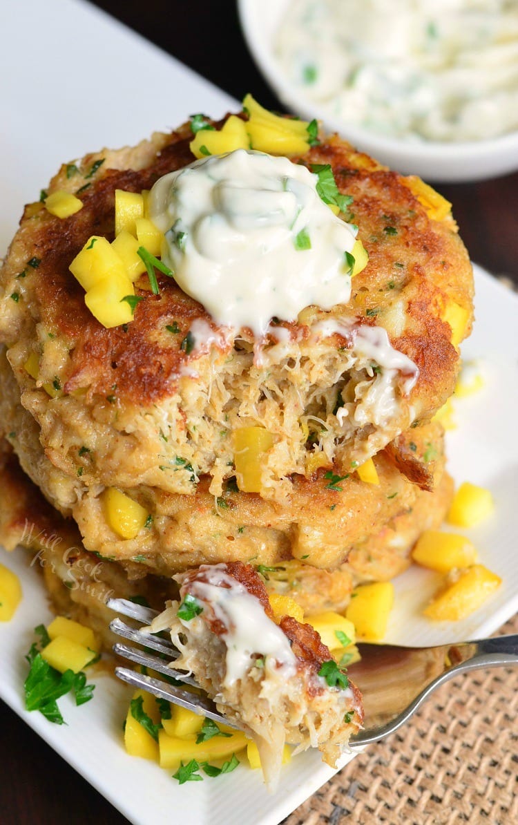 top view of Spicy Mango Crab Cakes stacked on a plate with sour cream on top and diced mango and parsley on the plate with a fork