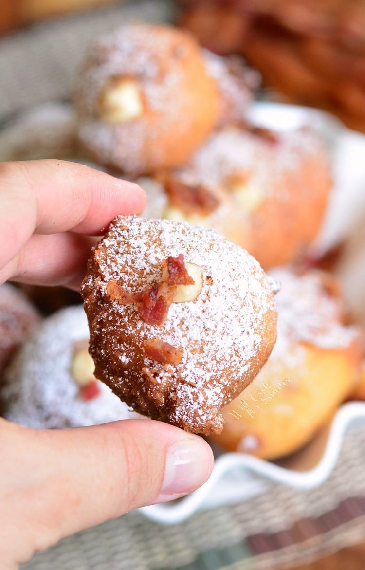holding a Bacon Brown Sugar Cream Doughnut Hole with a bowl of donuts in the background