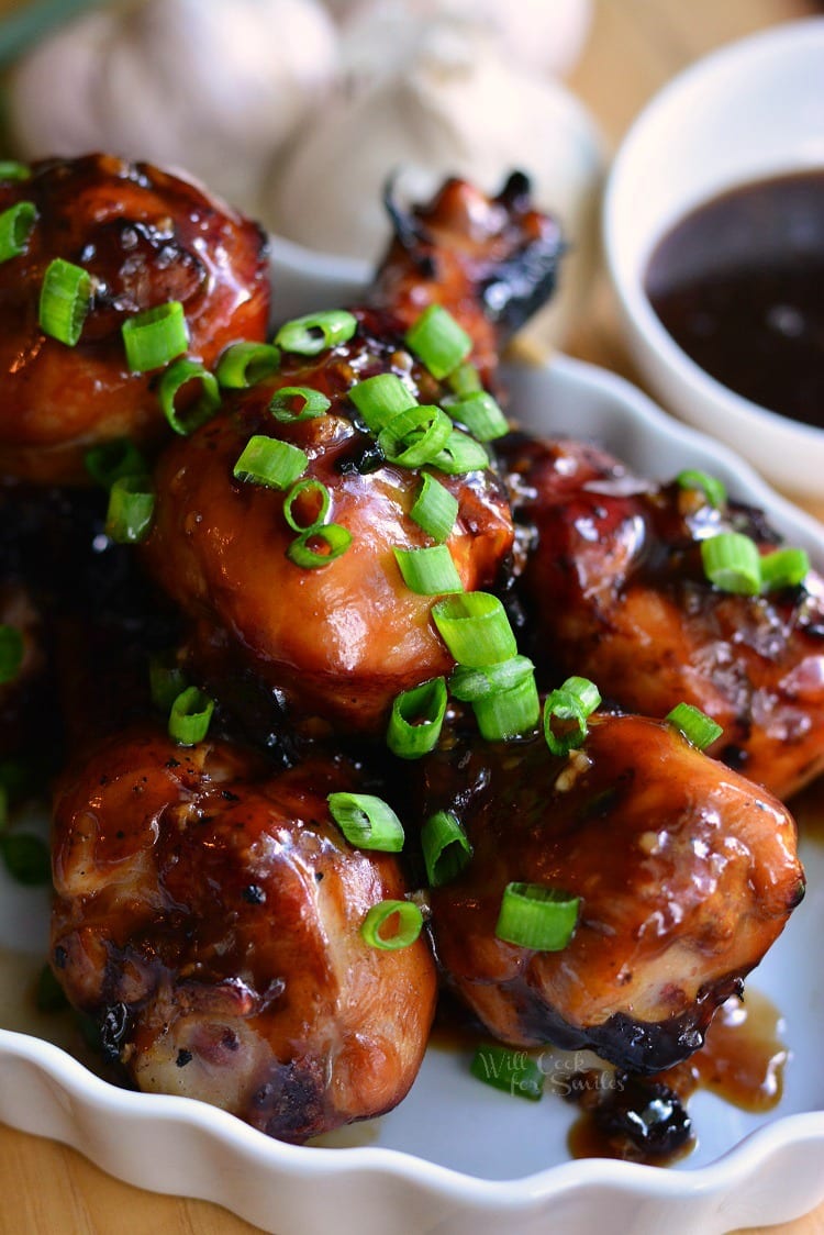 Sweet Garlic Grilled Chicken Drumsticks on a serving plate with garlic and sweet garlic sauce in a bowl in the background