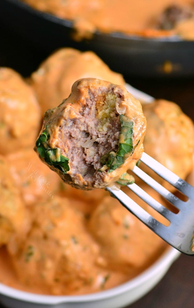 meatball on a for with a bite taken out and the rest of the meatball sin a bowl in the background