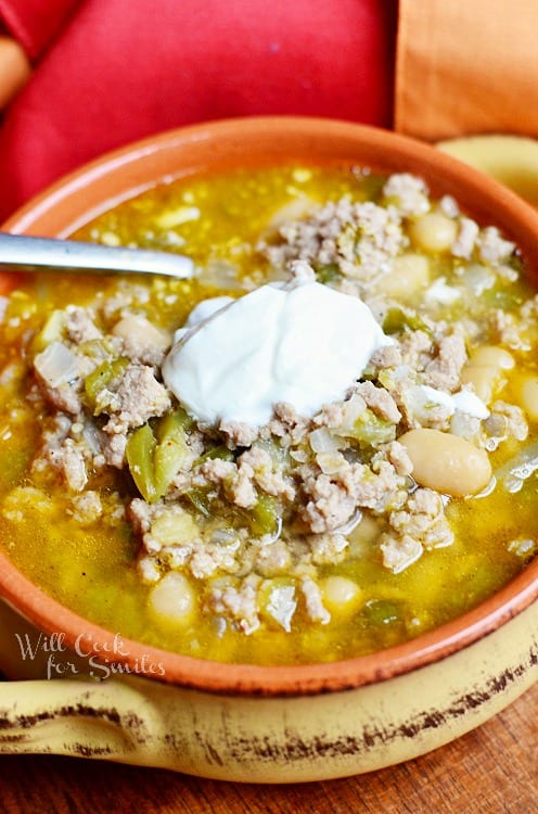 white turkey chili in a yellow and orange bowl with sour cream on top and a spoon in the bowl on a wood table