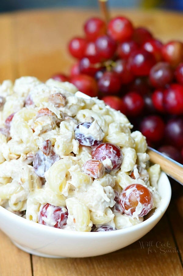 a bowl full of chicken and macaroni salad next to a bunch of grapes.