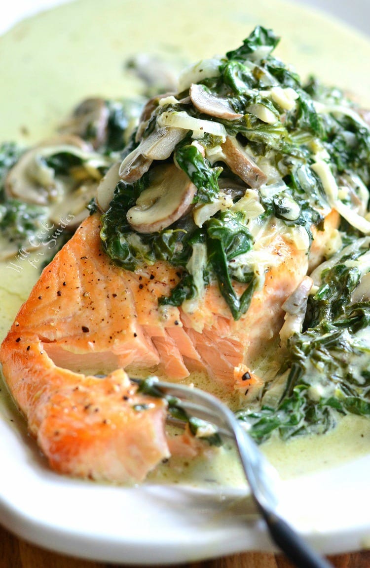 salmon Florentine with spinach and mushroom on a plate with bite of spinach on a fork.