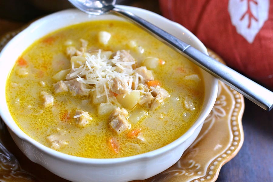 Creamy, Chunky Turkey Potato Soup with cheese on top in a bowl that is on a brown plate with a spoon across the bowl
