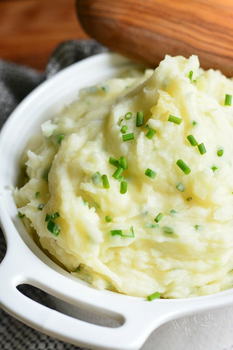 White Cheddar and Chive Creamy Mashed Potatoes in a serving bowl with a wooden spoon