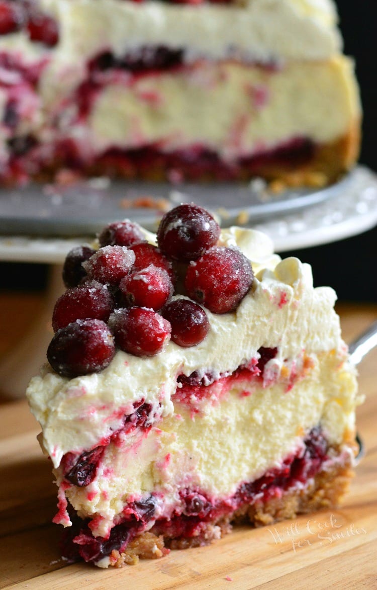 Christmas Cheesecake slice on a wood cutting board with cheesecake on stand in background