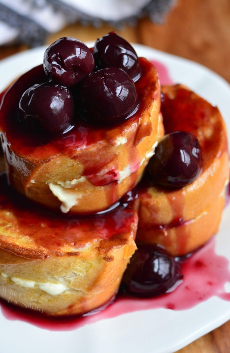 Cherry stuffed french toast stacked on a plate with cherries on top.
