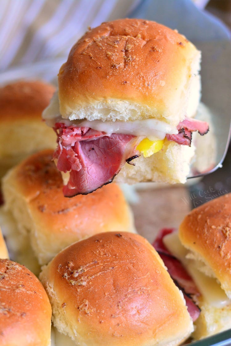 Hot Pastrami Sliders on a baking sheet with one being lifted out with a spatula