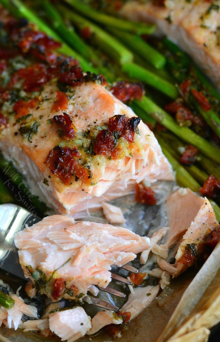 Sun Dried Tomato Lemon Baked Salmon and Asparagus in parchment paper on a baking sheet