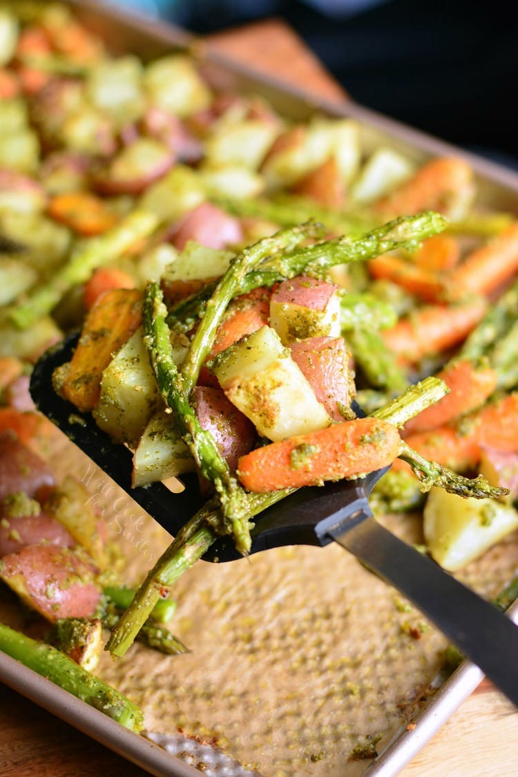 Pesto Roasted Potatoes Carrots and Asparagus on a baking sheet with a spatula lifting some out