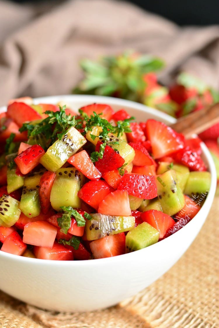 strawberry and kiwi in a fruit salad with mint on top.
