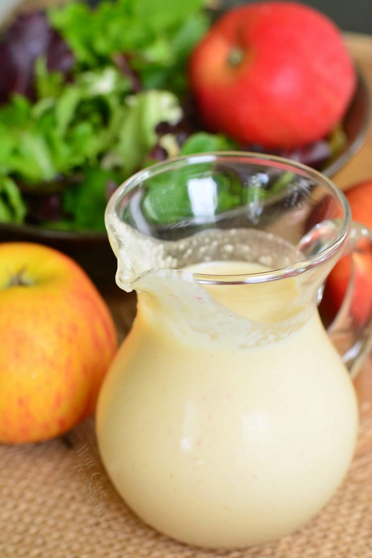 Delicious homemade Apple Vinaigrette in a glass container on a wood table with apples and salad in the background