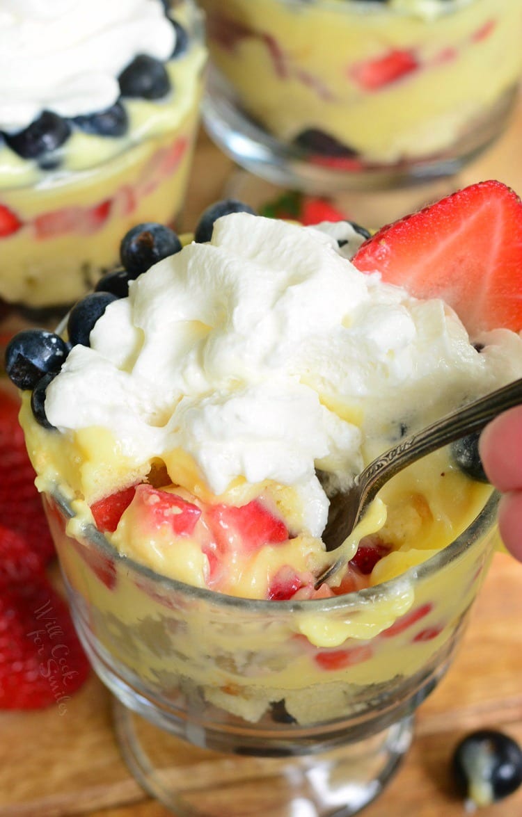Easy Coconut Berry Trifle in a glass serving bowl with a spoon on a cutting board with a strawberries