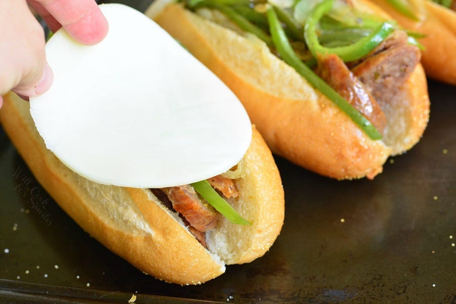 putting cheese on Philly Cheese "Steak" Sausage Hoagies on a baking sheet