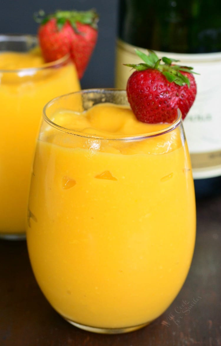 Mango Champagne Slushies in a champagne glass with strawberries on the edge.
