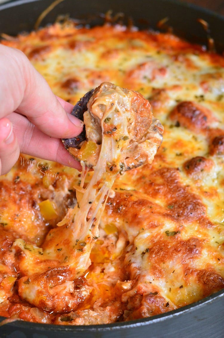 lifting some Cheesy Meatball Dip with a chip out of the pan.