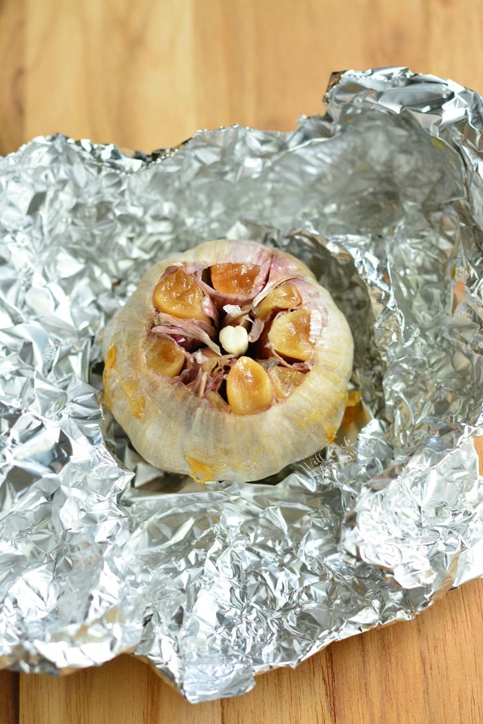 roasted garlic laying on tin foil on a wood cutting board