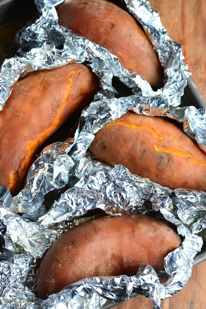Baked Sweet Potatoes laying in tin foil on a cutting board