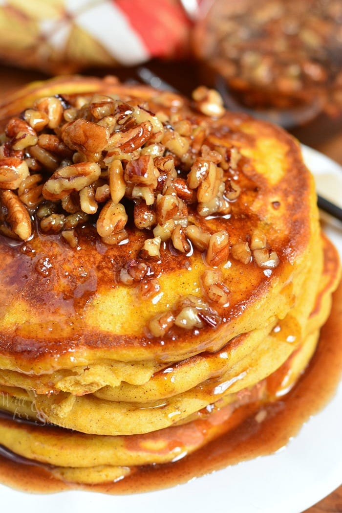 pumpkin pancakes stacked on a plate and topped with pecans and syrup.