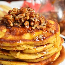 a stack of several pumpkin pancakes topped with cinnamon pecan syrup.