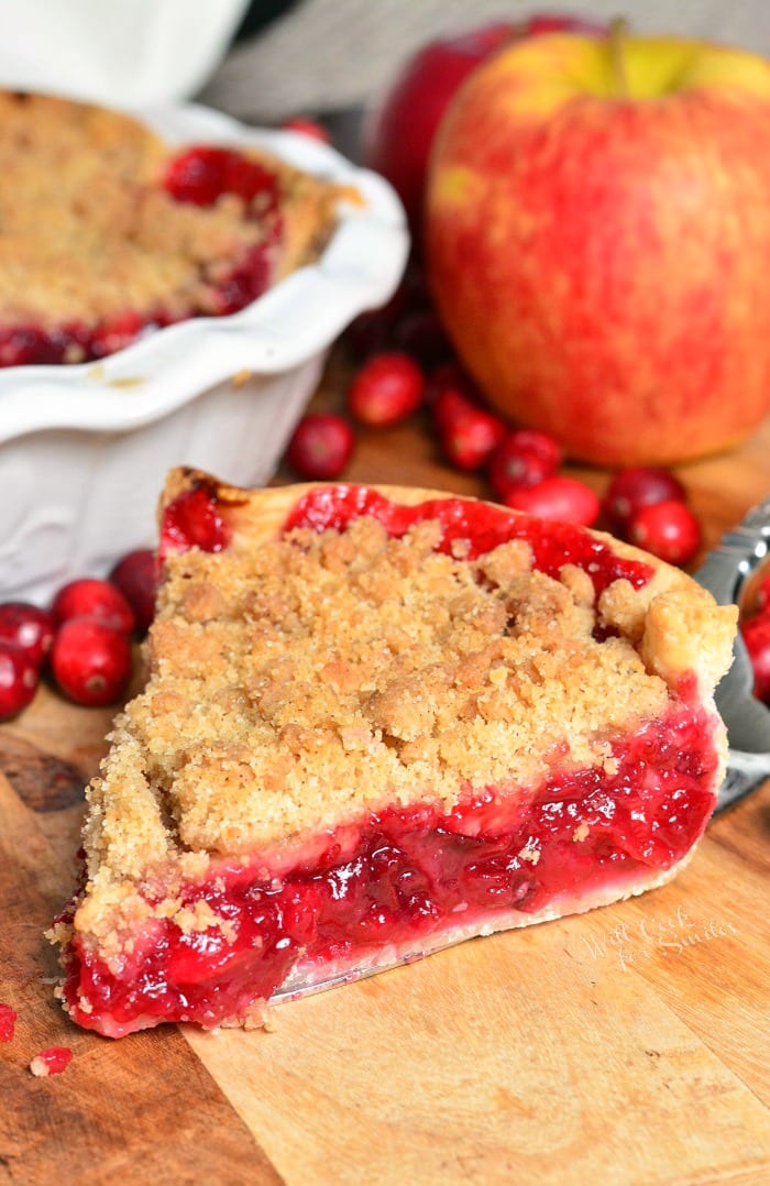 Apple Cranberry Pie on a wood cutting board with cranberry and apples in the background