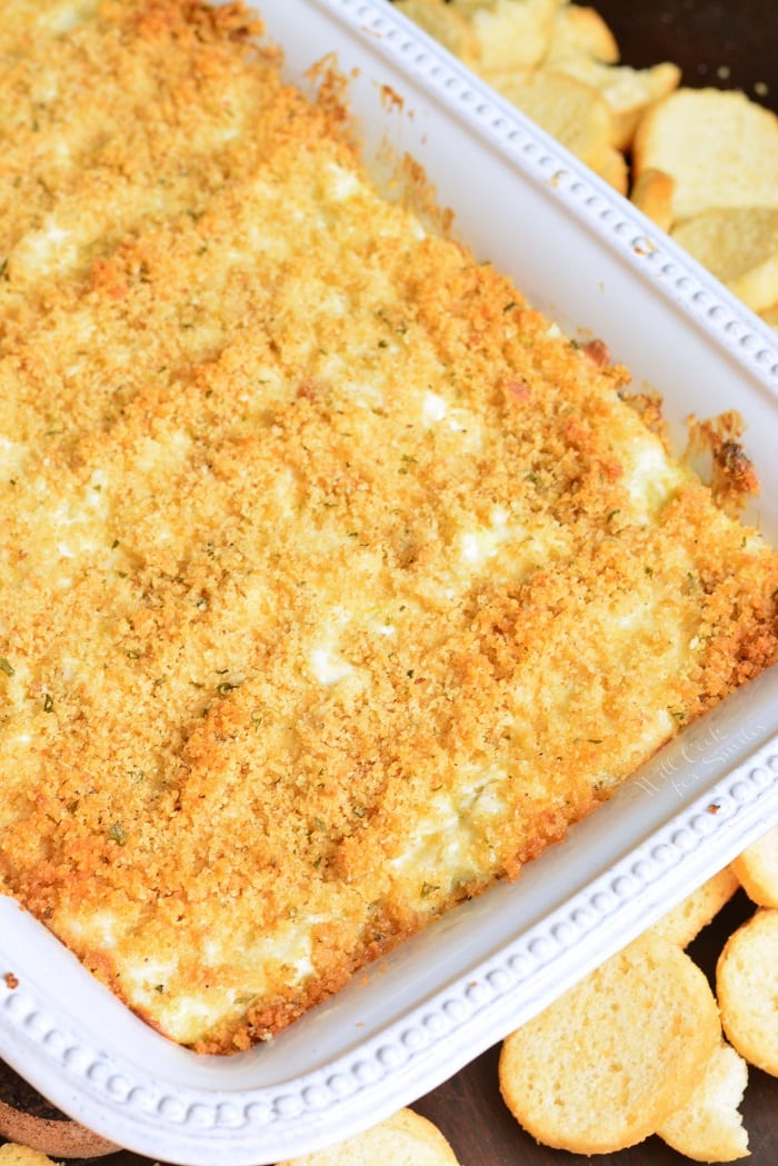 baked creamy and cheesy crab artichoke dip in a white baking dish.