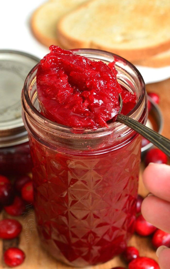 Cranberry Jam in a mason jar with a spoon lifting a spoon full out