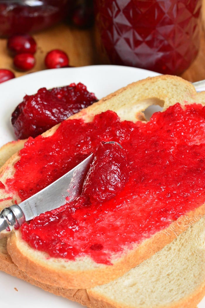 spreading Cranberry Jam on toast with a butter knife that is on white plate