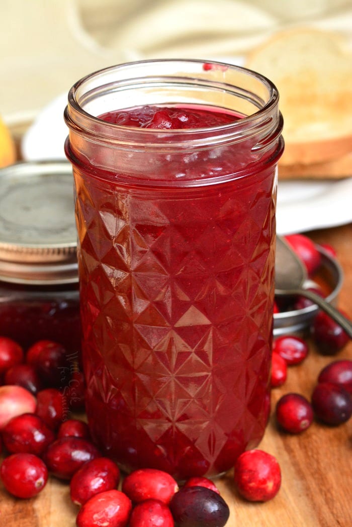 Cranberry Jam in a mason jar on a wood cutting board and fresh cranberries around it