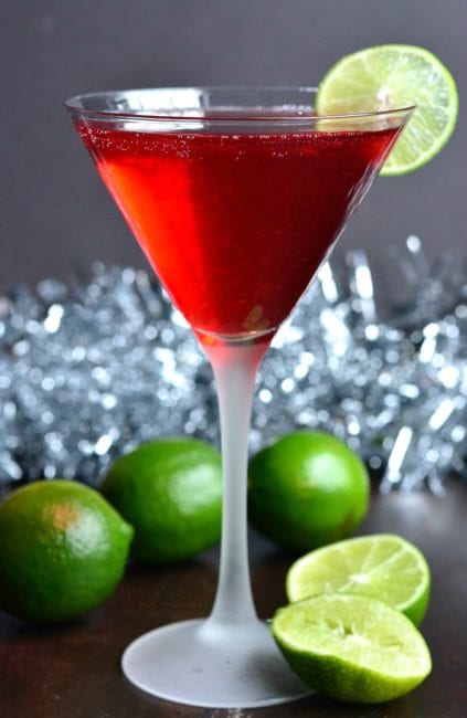 tall glass with red cocktail lime slices around and sparling garland