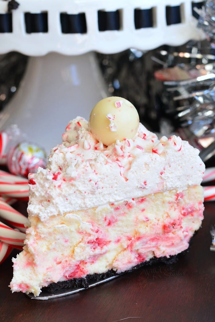 piece of Peppermint Cheesecake on a wood table with candy cans and cake stand in the background