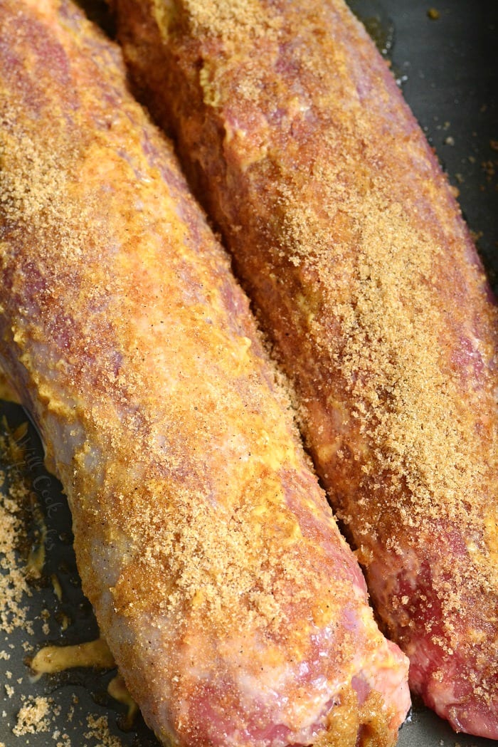 uncooked pork tenderloins side by site in a roasting dish with seasoning over it.